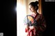 A woman in a kimono holding a fan in front of a window.