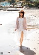 A woman walking on the beach wearing a white dress and a pink cardigan.