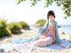 A woman in a blue and pink dress sitting on a beach.