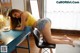 A woman in a yellow top and denim shorts sitting at a desk.