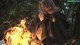 A woman sitting in front of a bonfire in the woods.