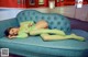 A woman in a green bodysuit laying on a blue couch.